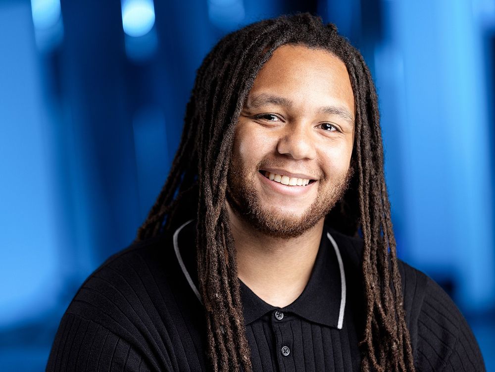 Confident male actor with long dreadlocks smiling against a blue background, professional acting headshot in Atlanta studio.