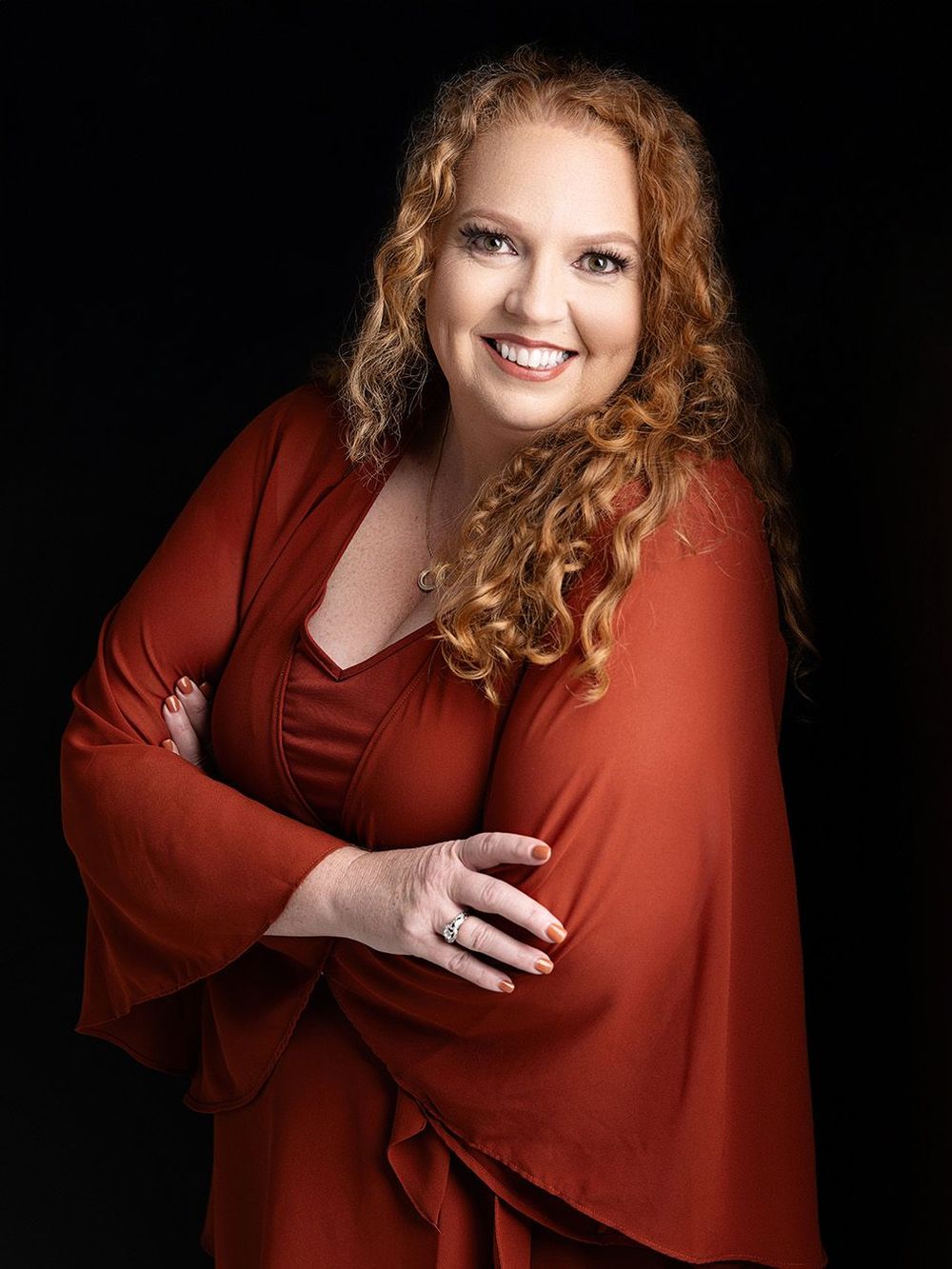 Confident female executive in red dress against black background, luxury Atlanta headshot photography.