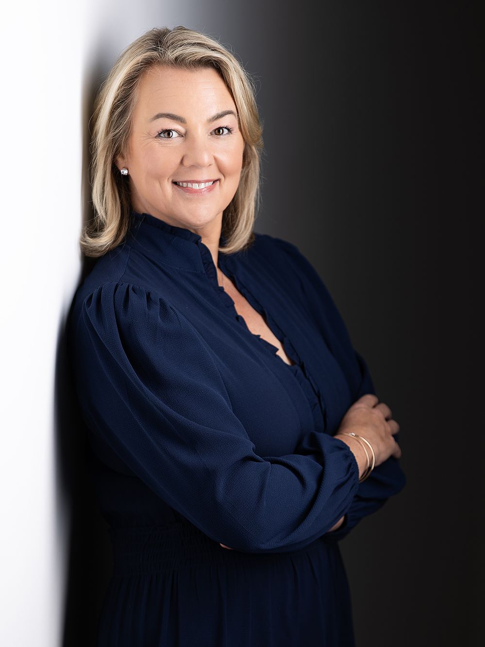 Professional headshot of a person in a navy blue blouse smiling warmly against a dark background.