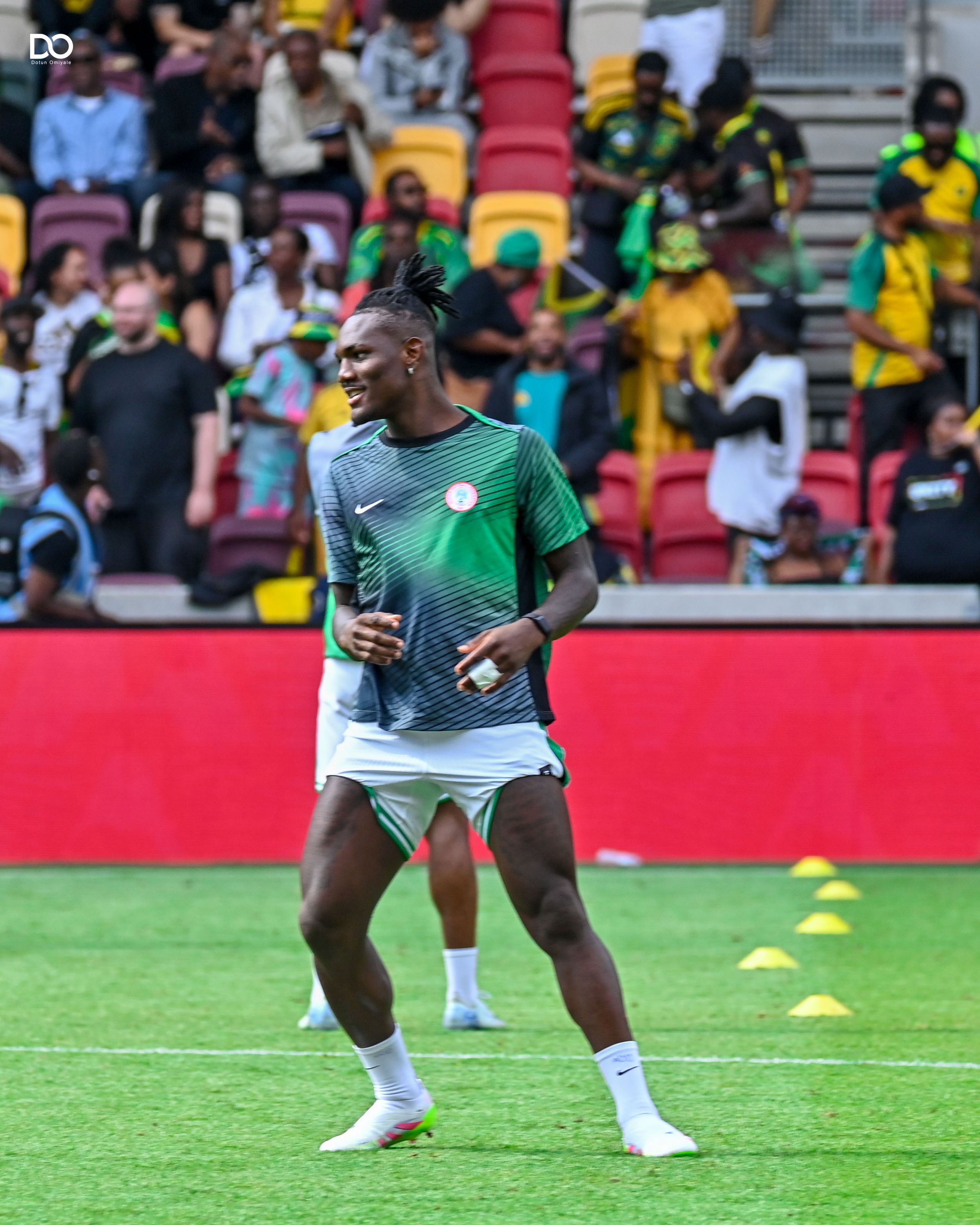 Soccer players in green and white uniforms warming up on a field with stadium seating visible.