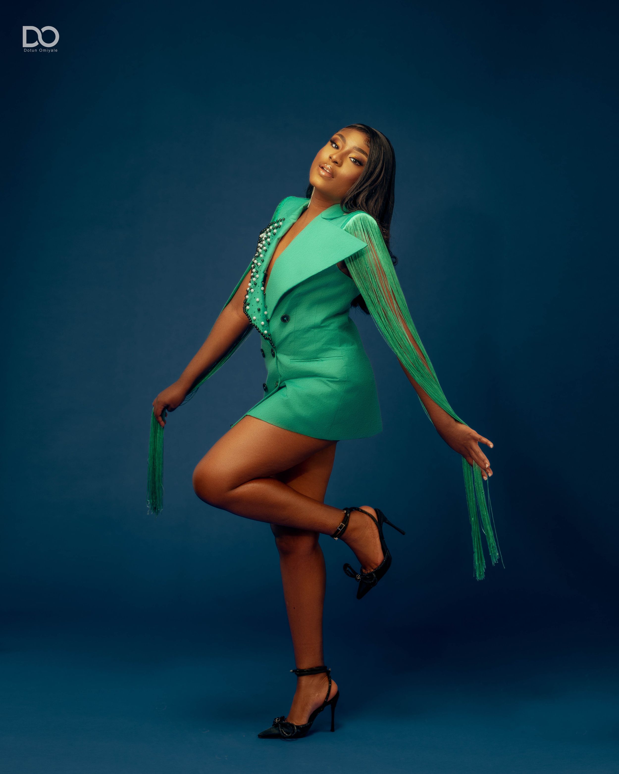 Dynamic fashion poses in emerald green outfit against dark studio background.