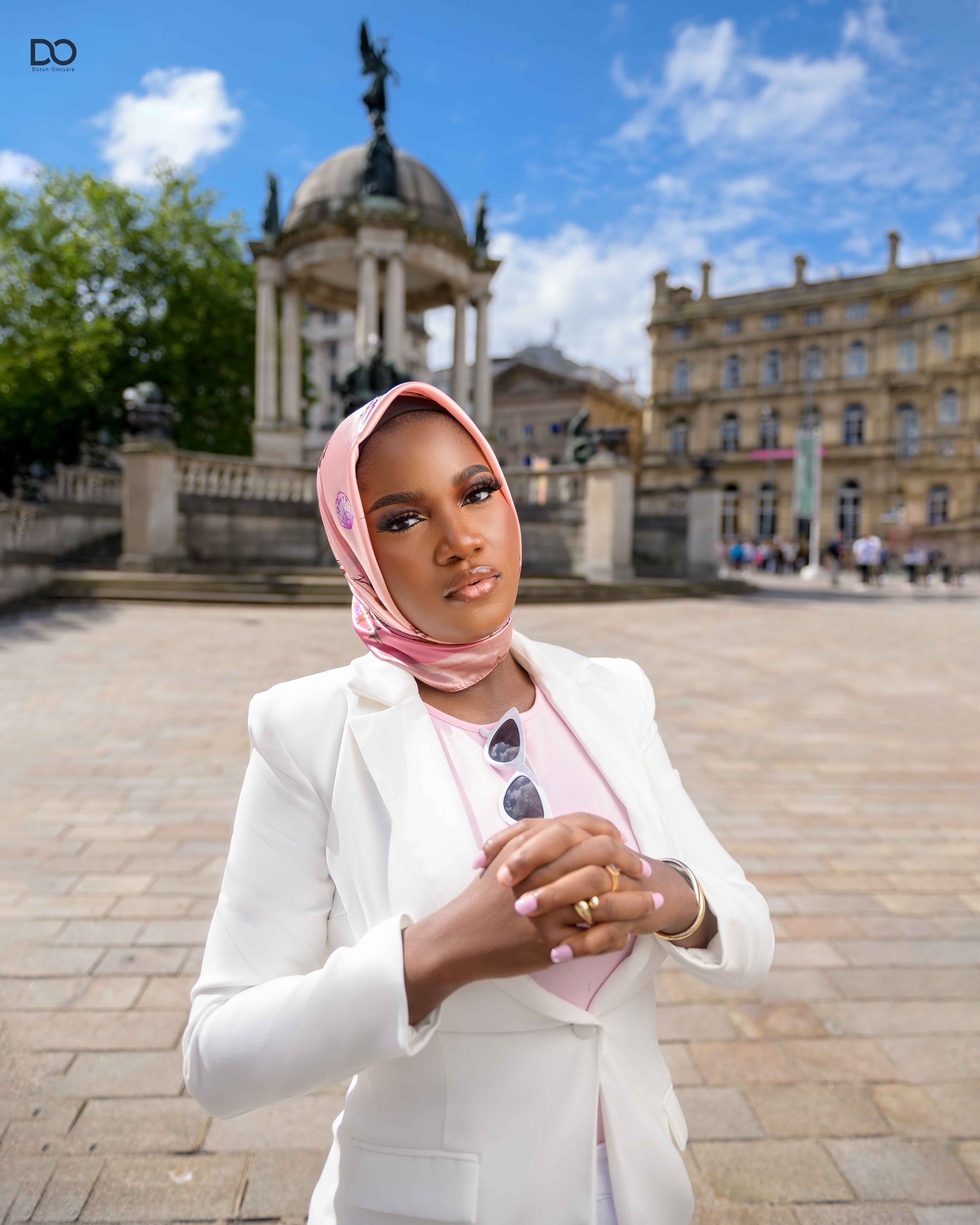 Professional portrait featuring a person in a white blazer and pink hijab standing in front of historic European architecture.