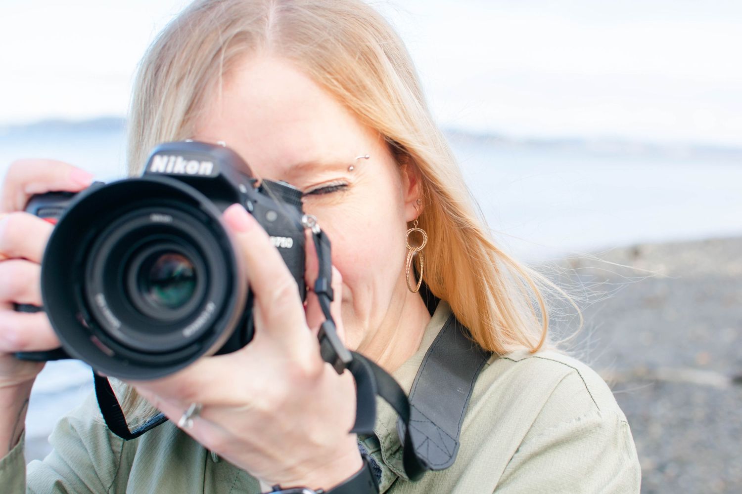 Close-up of person holding professional Nikon camera against beach background.