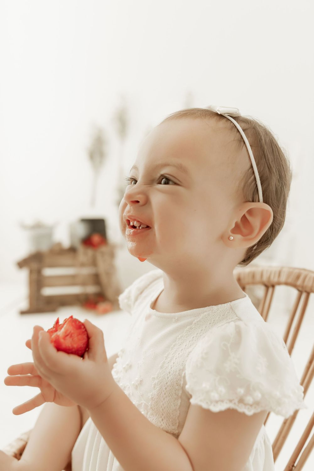 A young child in a white dress smiles while holding a red apple in their hands.