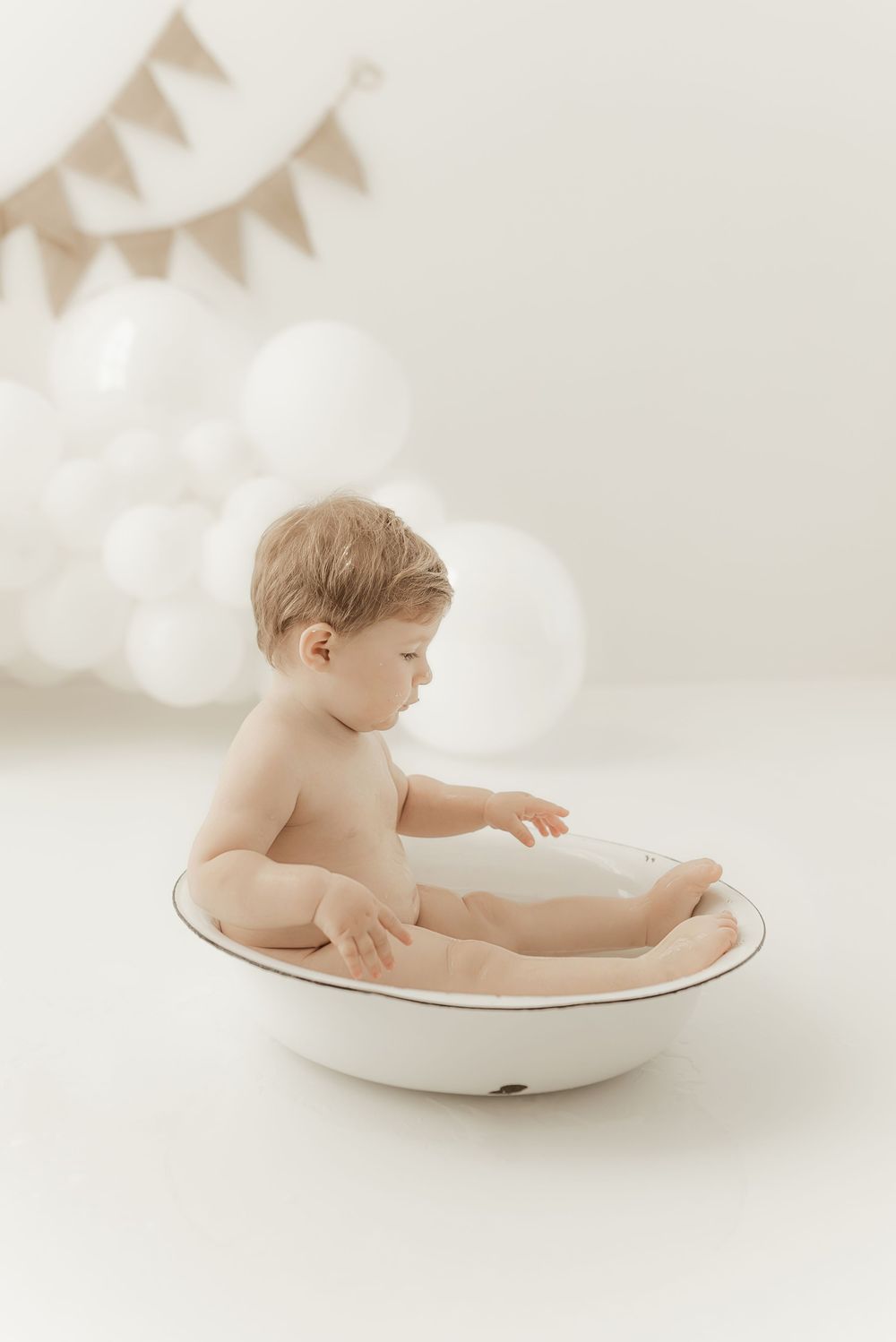 Gentle baby bath portrait with soft bunting flags in background and dreamy white lighting.