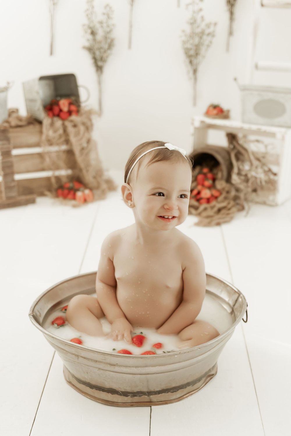 Sweet milk bath photography setup with rustic decor, strawberries and vintage metal tub on white wooden floor.