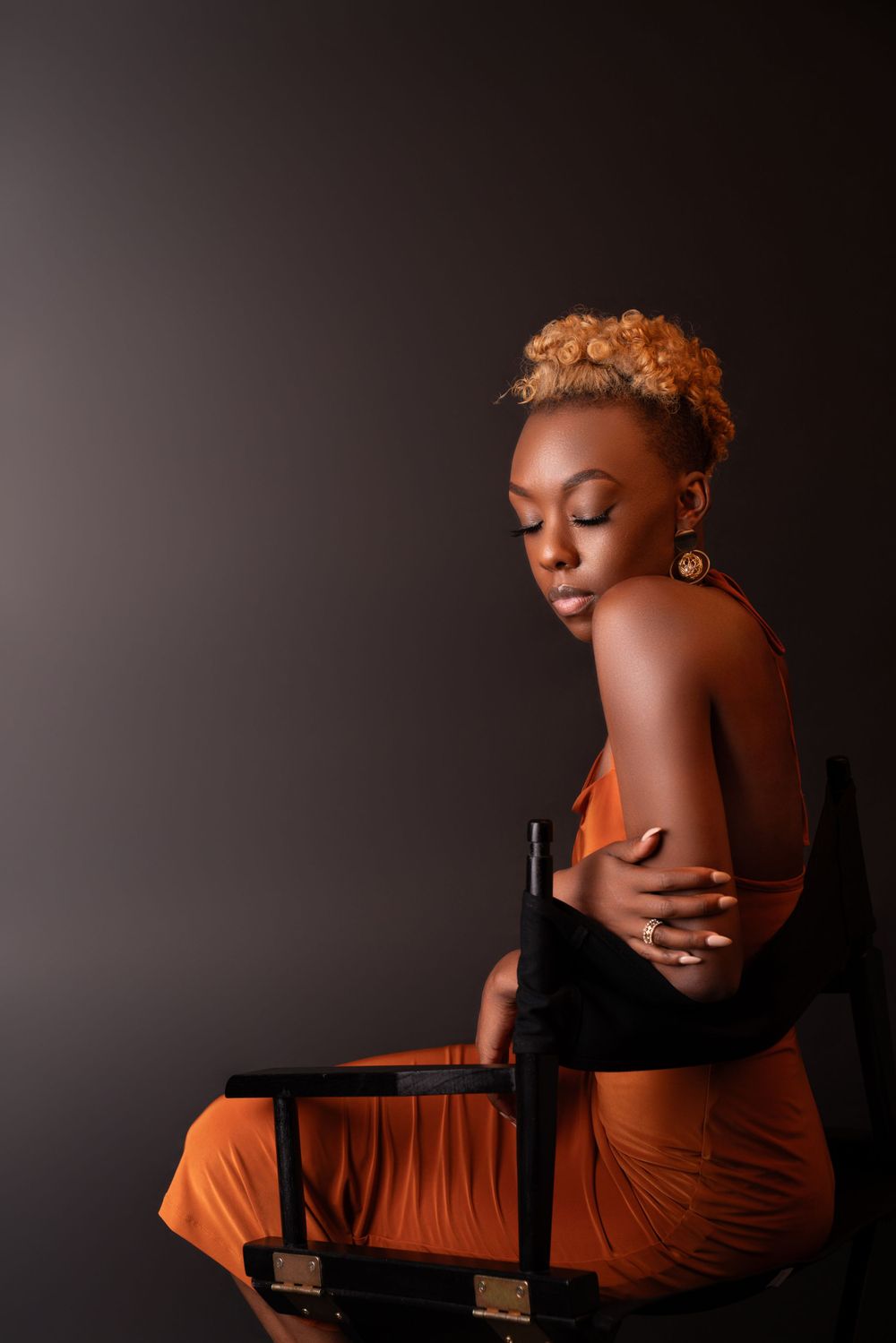 Artistic portrait of model in orange dress against dark background showcasing elegant pose and style.