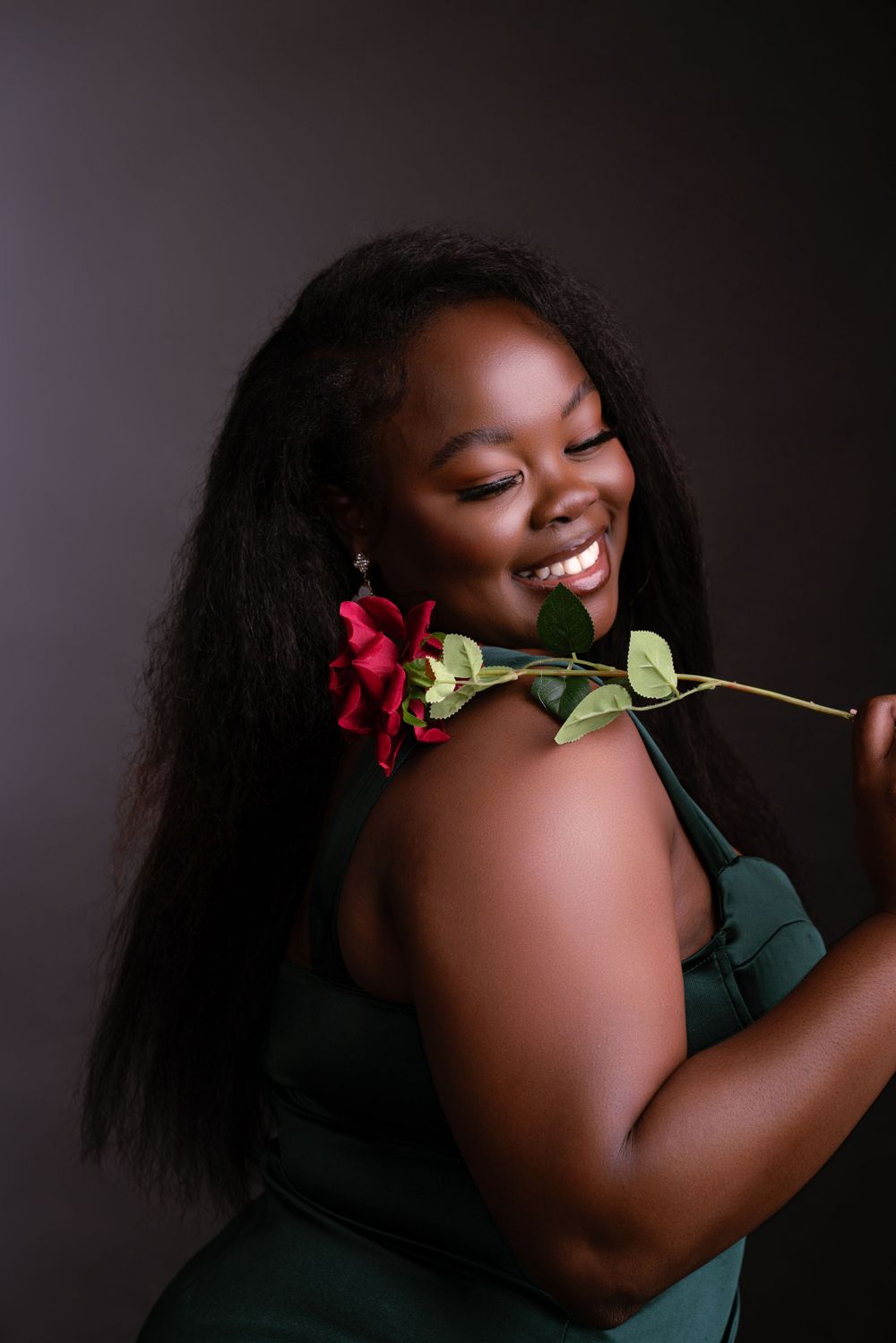 A joyful expression radiates as someone holds a beautiful red and green rose against a dark studio background.