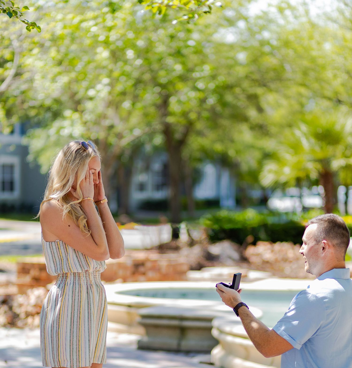 Surprise marriage proposal scene by fountain in garden setting.