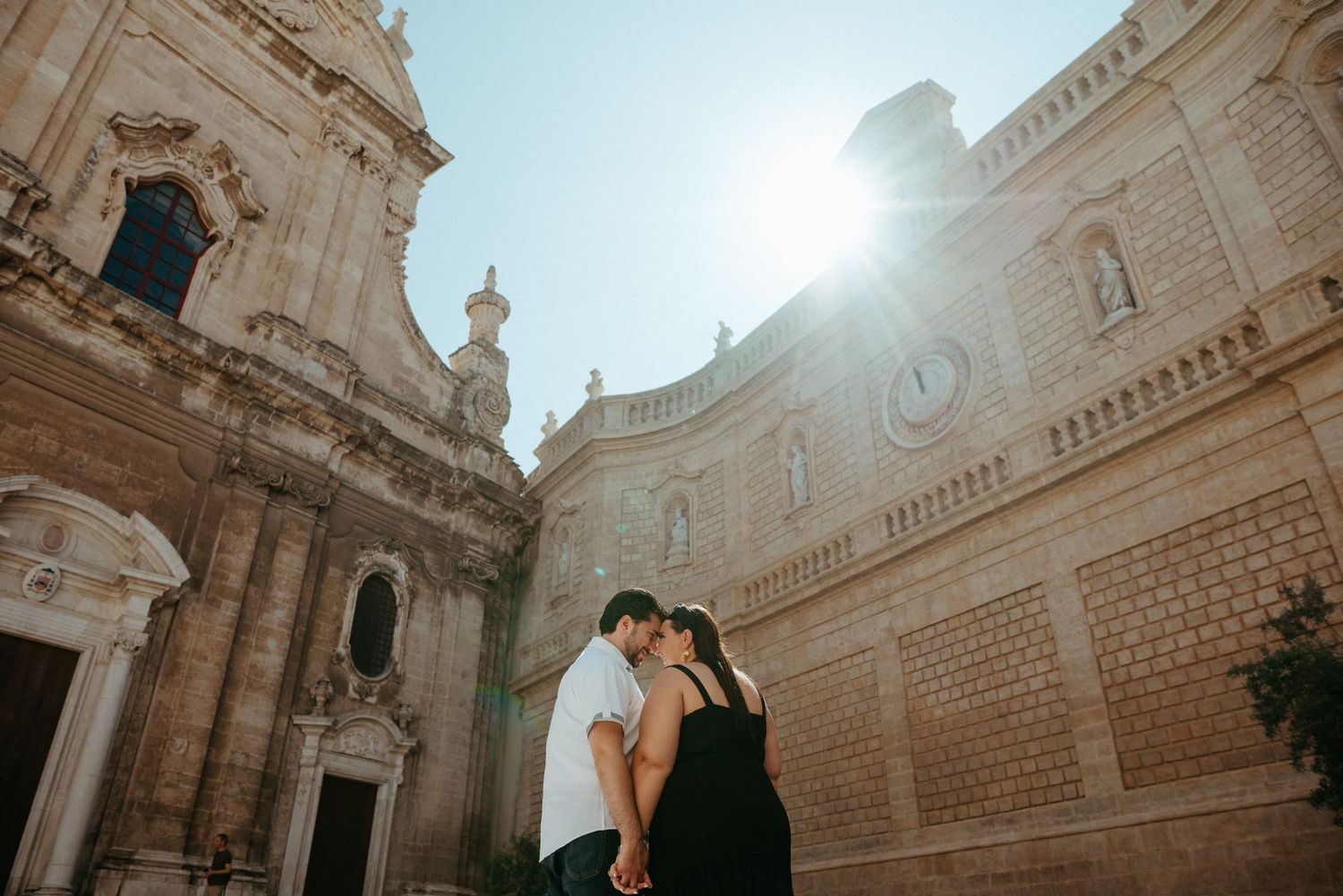 Sun-drenched wedding photo in front of an ornate Italian church facade.