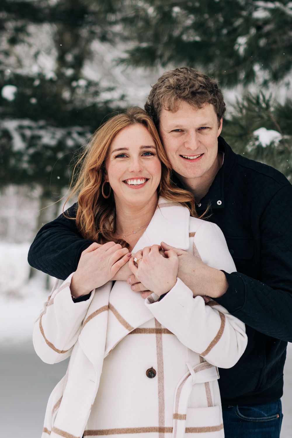 Happy couple shares embrace in snowy forest wearing contrasting black and white outerwear.