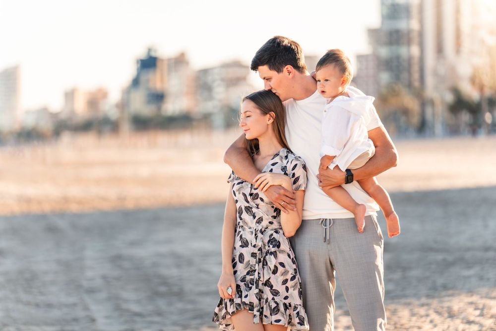 family of 3 on sandy beach cuddling and looking content and happy for family photos in Alicante Playa San Juan