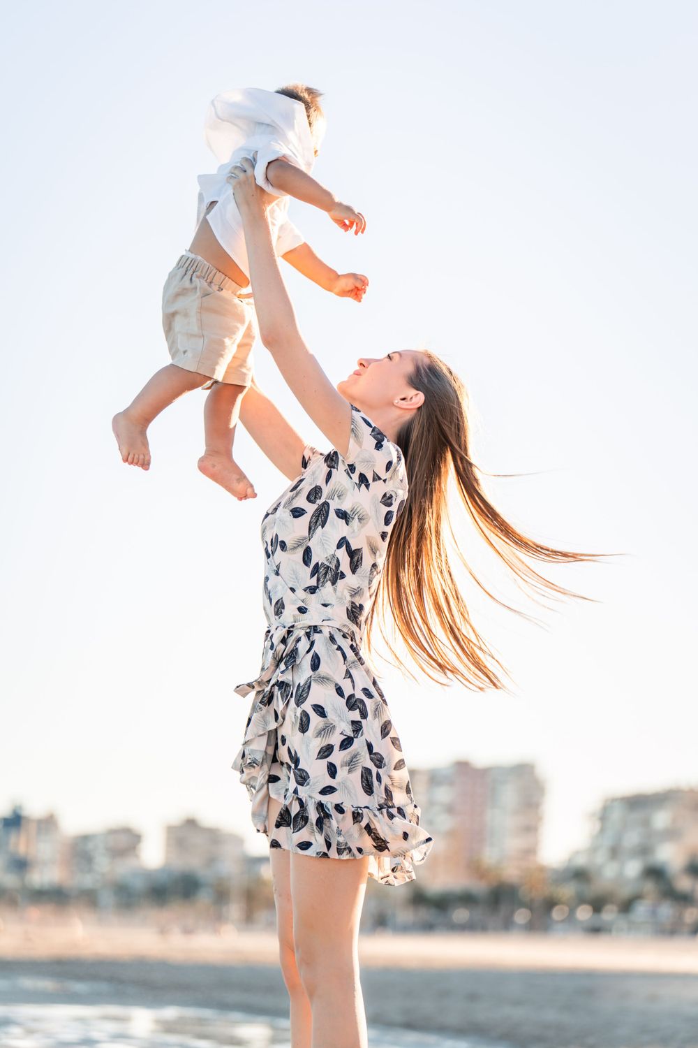 mom throwing son in the air on sunny beach in Alicante, beautiful blue sky day
