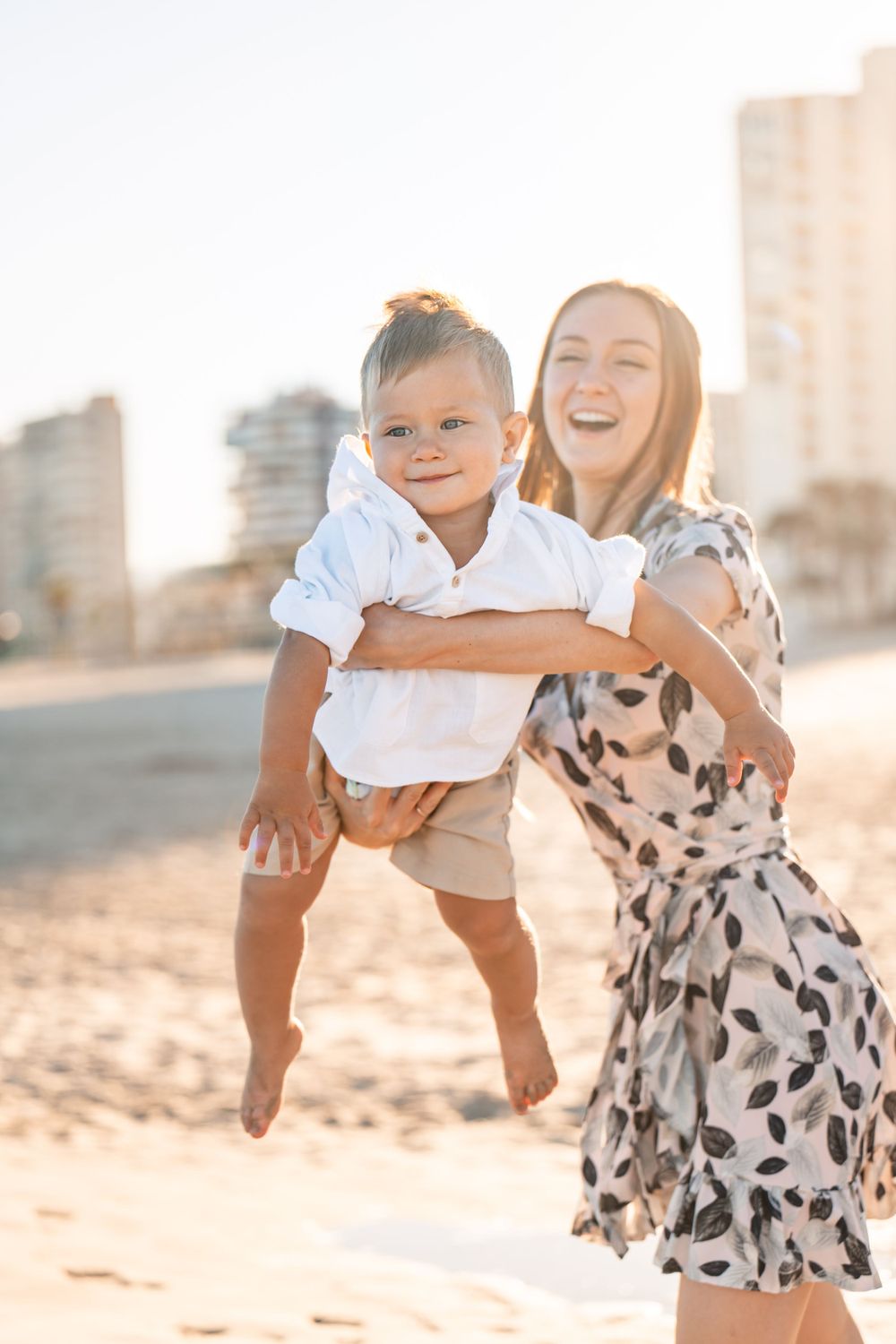 mom swinging son back and forth playing in the golden sun of late afternoon on the beach