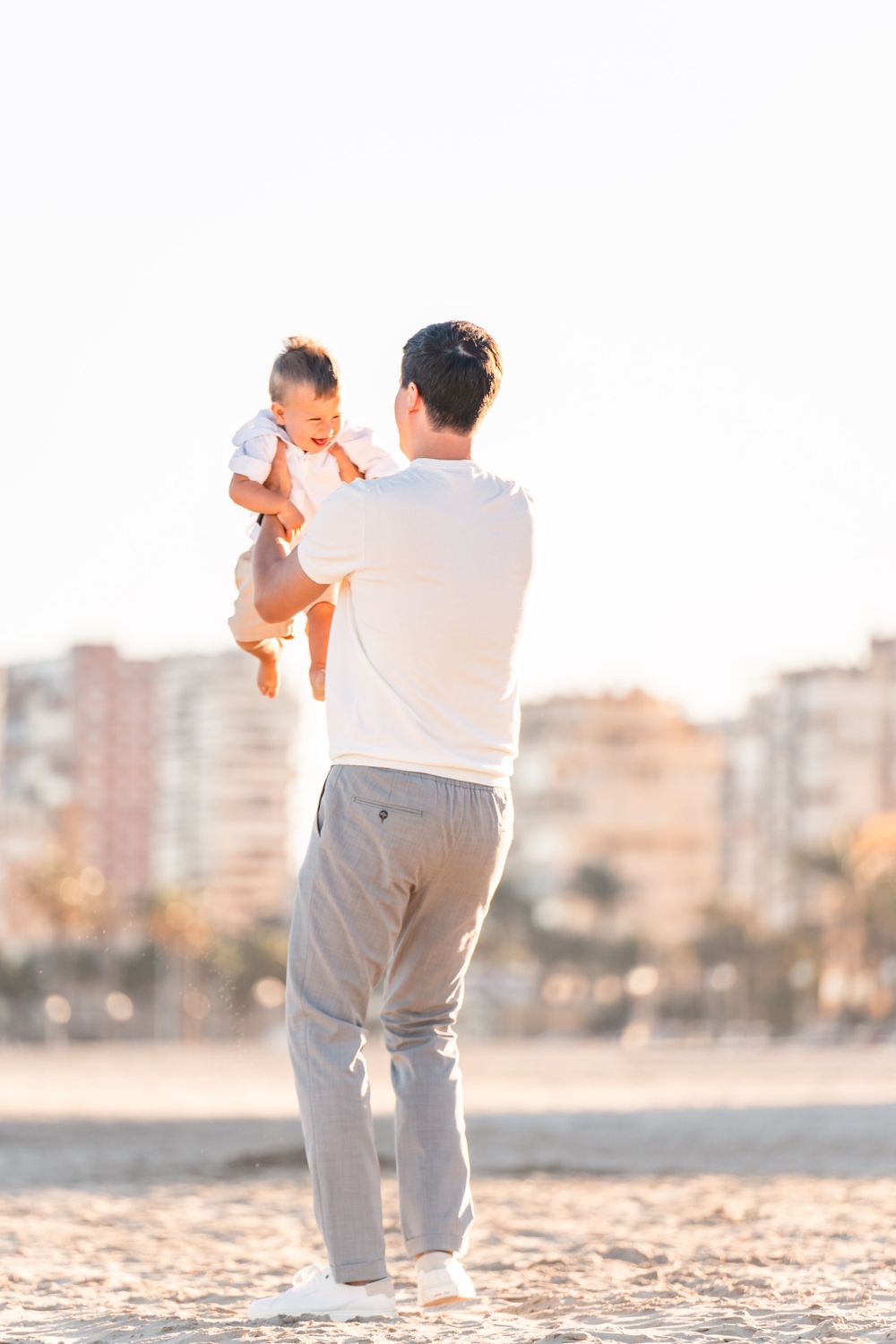 dad playing with son on the beach in late afternoon golden sun and swinging him and lifting him