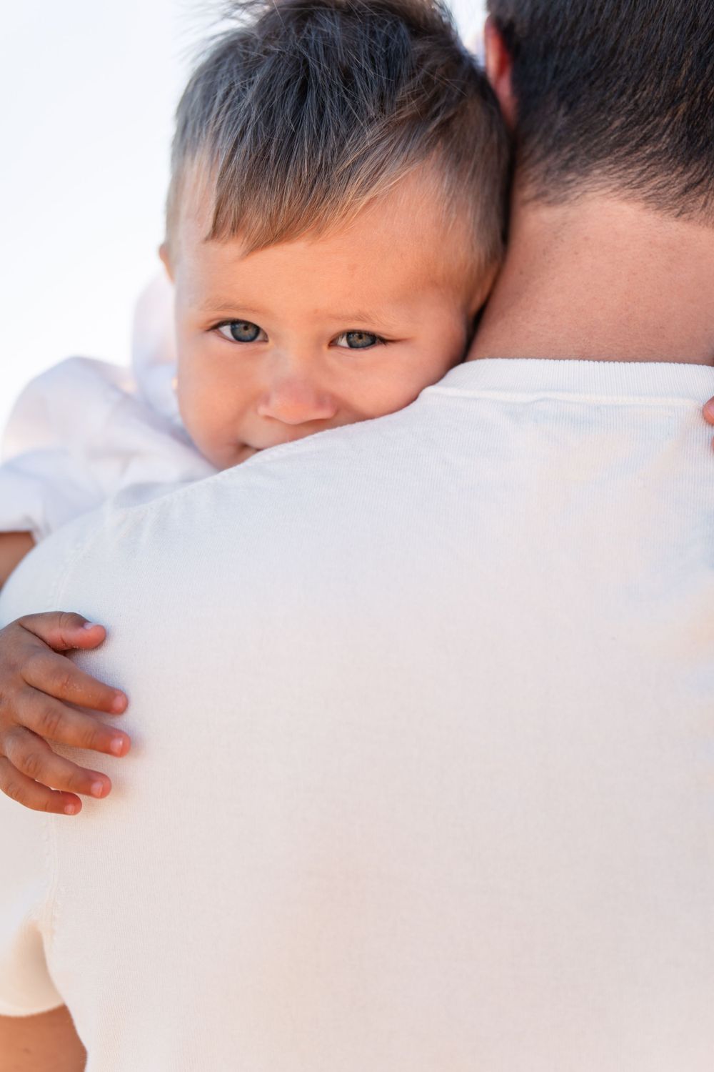 little boy cuddling on his fathers shoulder and peaking over for a photo