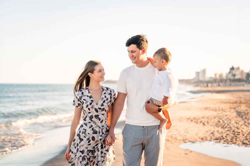 family of 3 on sandy beach looking at water in Alicante Spain at sunset golden hour