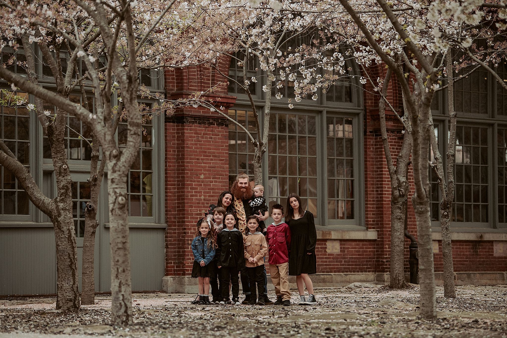 Family group portrait in front of a brick building with winter trees creating a scenic backdrop.