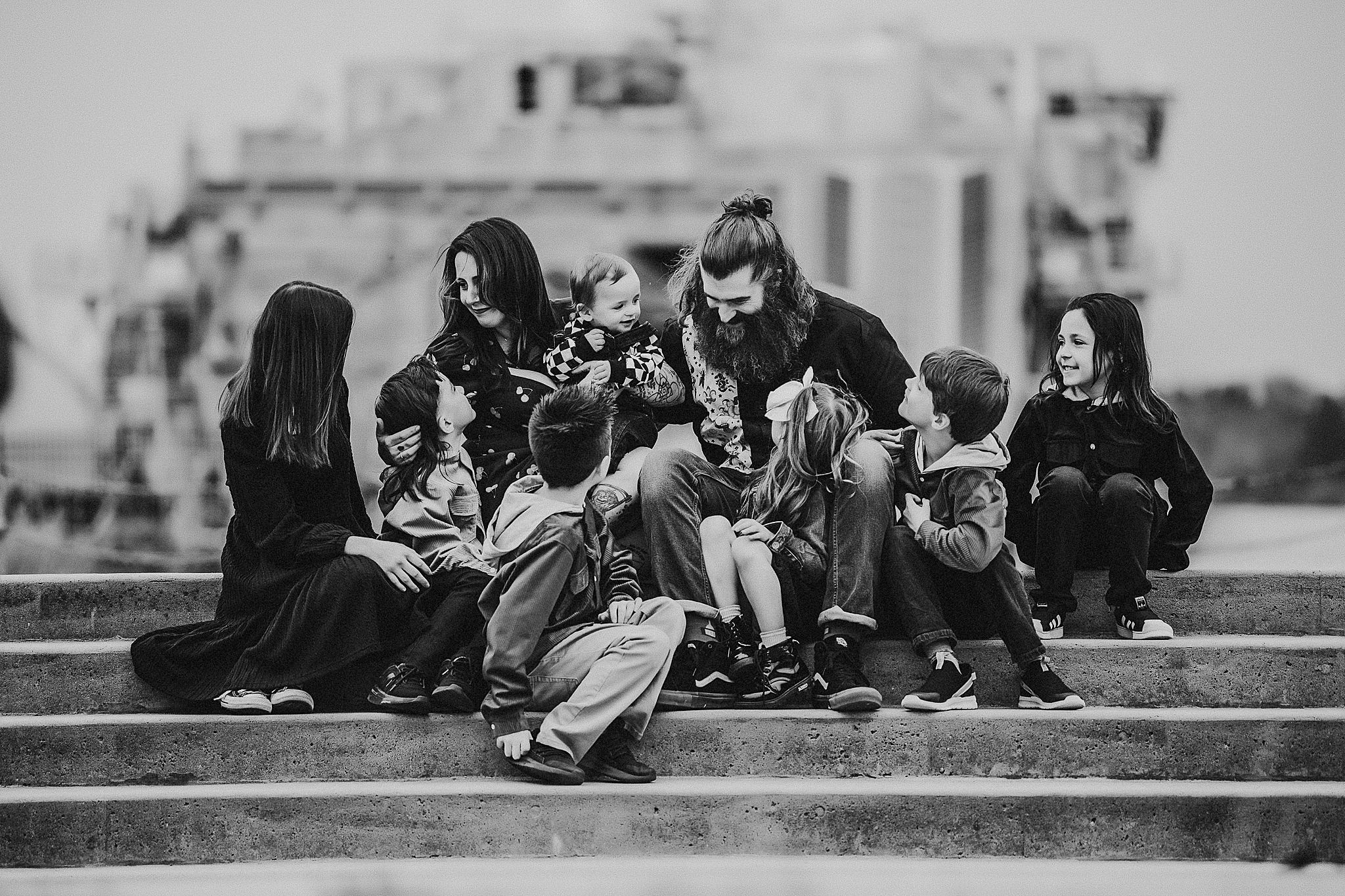 A group sits together on concrete steps in black and white with an industrial backdrop.