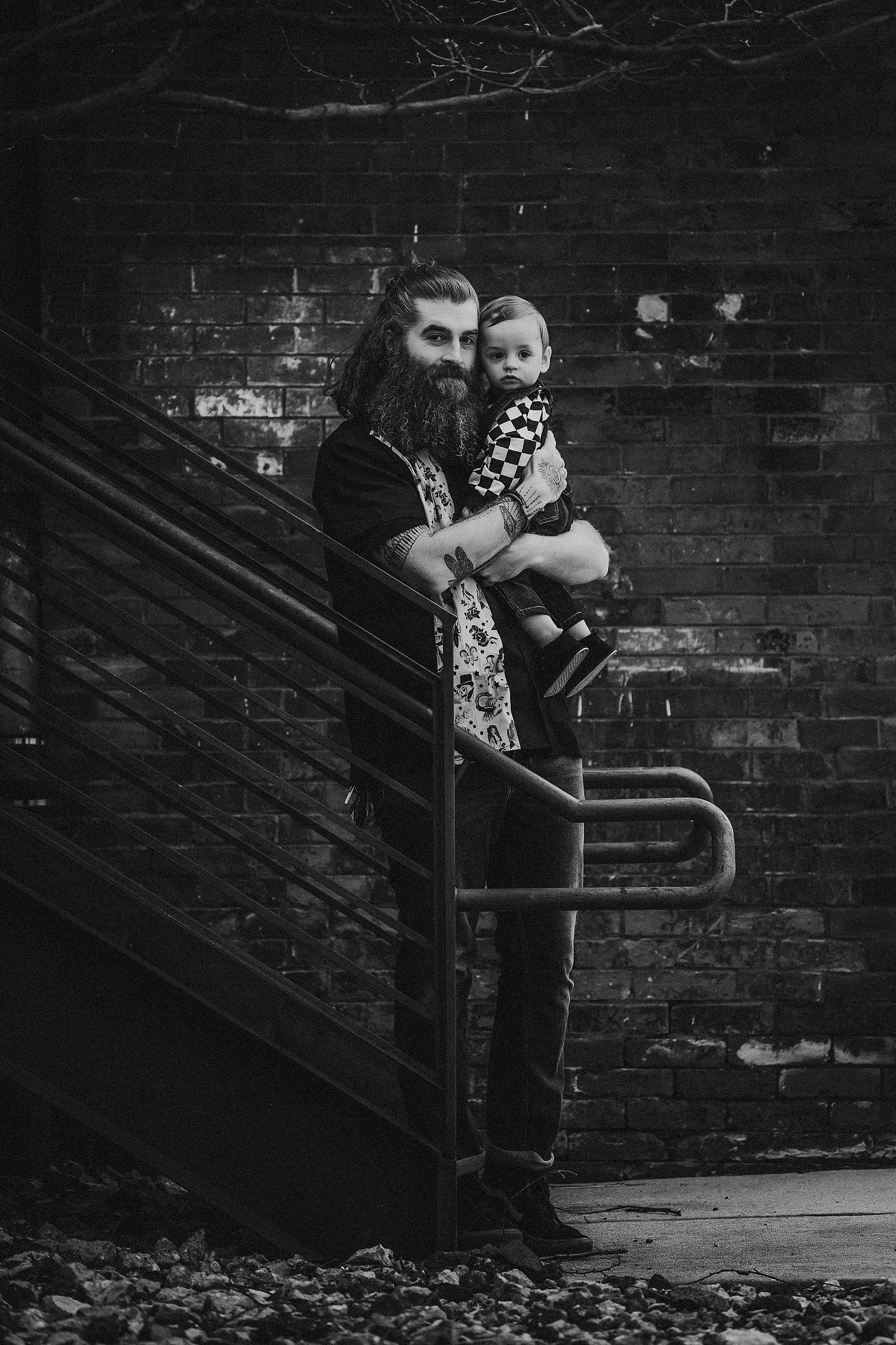 A dramatic black and white portrait on industrial stairs against brick wall background.