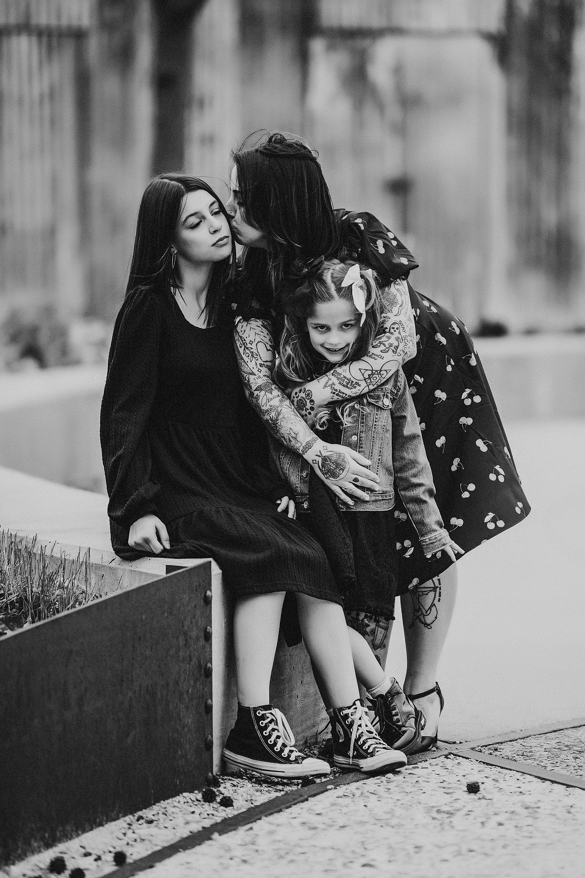 Three friends share a tender moment sitting together on an urban ledge in black and white.