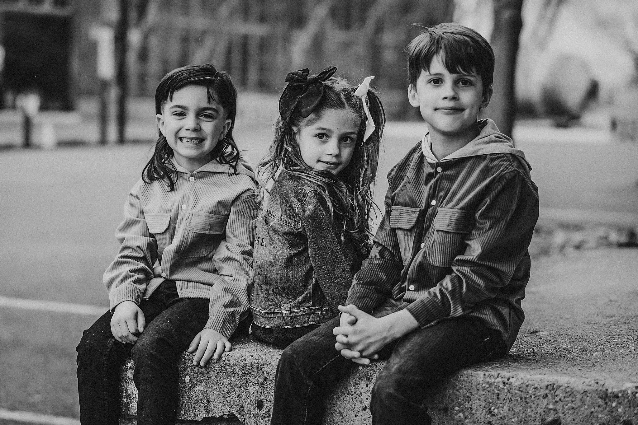 Black and white portrait of three children sitting together outdoors.