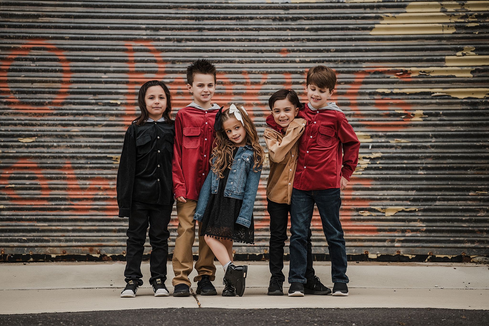 Group poses casually against an industrial metal garage door with graffiti.