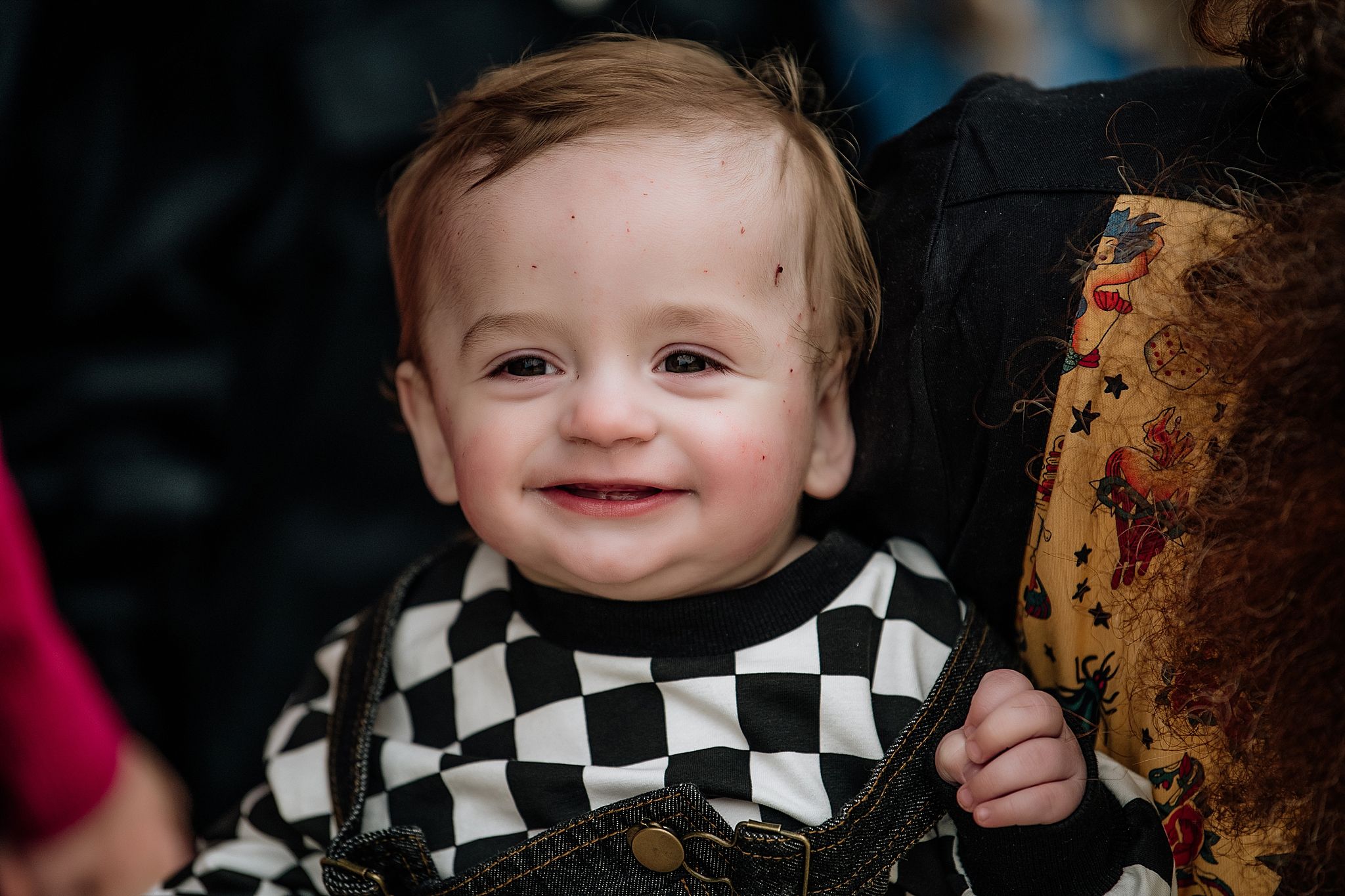 Baby wearing a black and white checkered outfit smiles brightly.