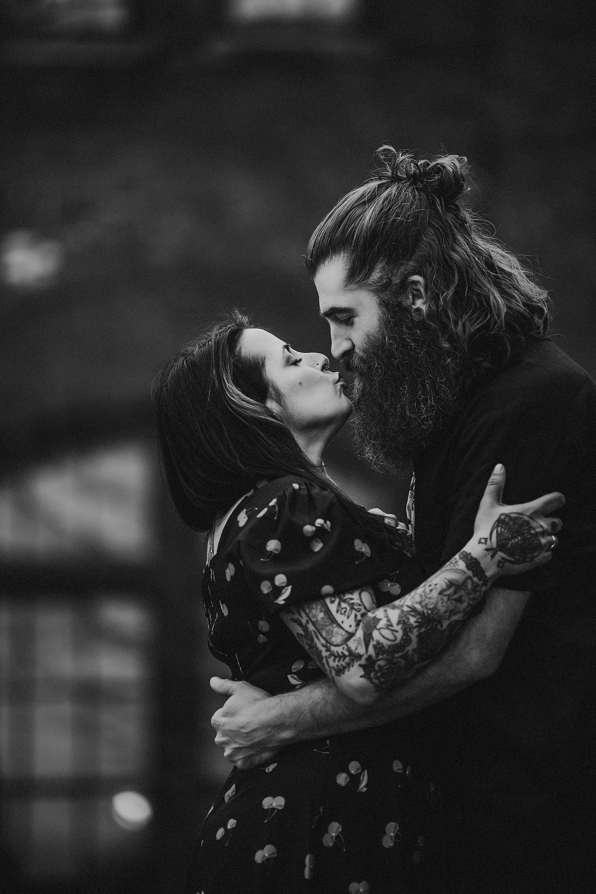 Black and white portrait of couple sharing an intimate embrace with visible tattoos and beard.