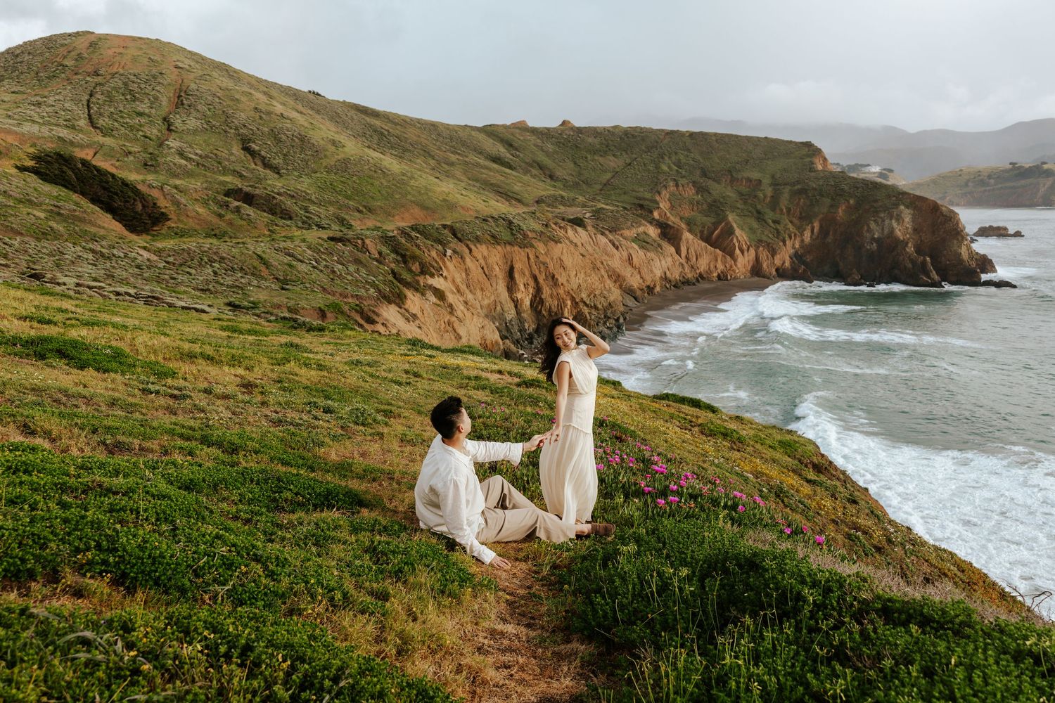 bride and groom running along clifftop field with ocean in the distance during san francisco elopement day
