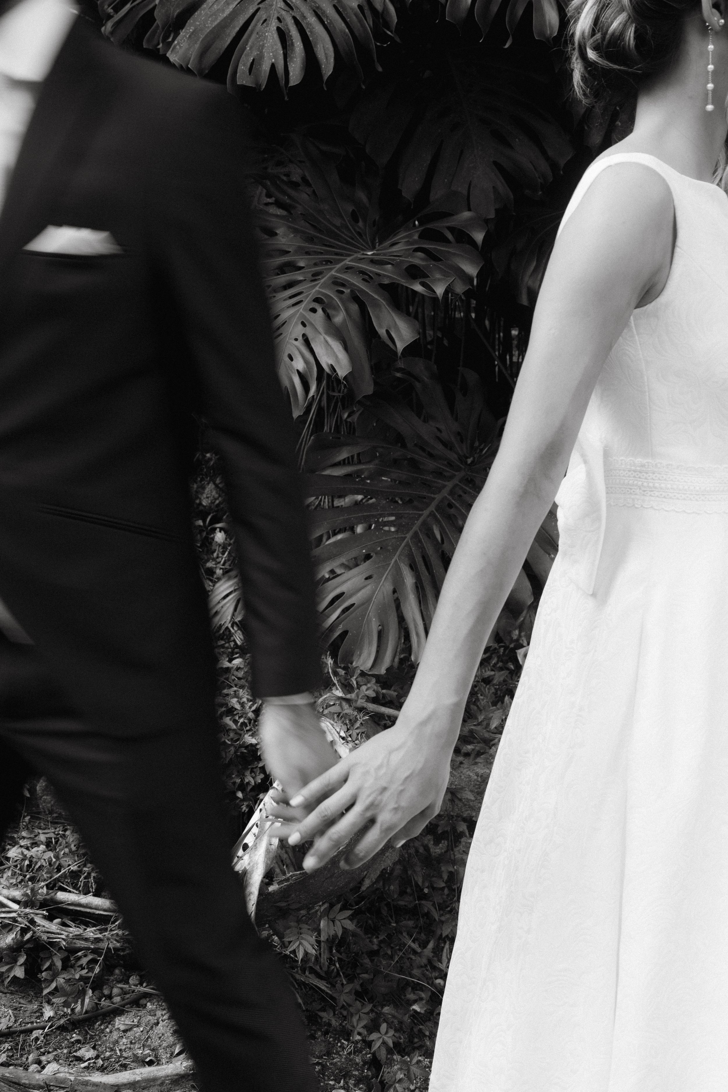 Black and white wedding portrait with dramatic monstera leaf backdrop.
