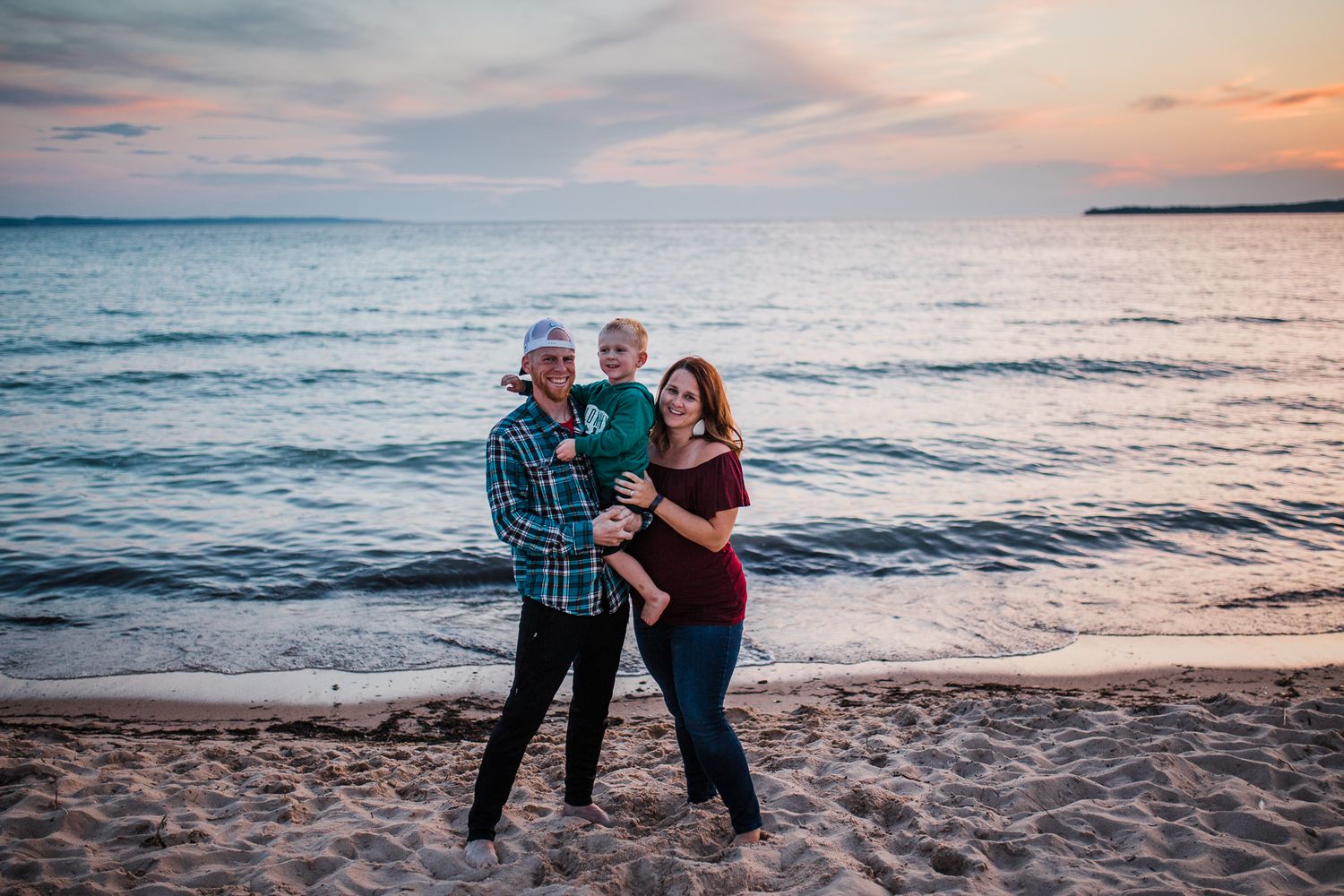 A family embraces on a sandy beach during a beautiful sunset by the ocean.