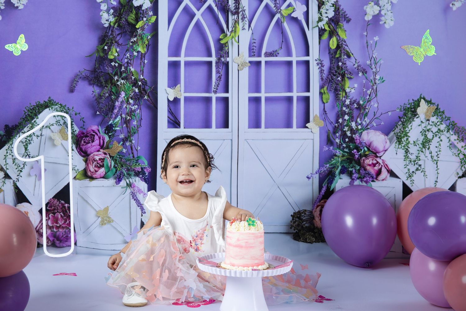 A whimsical purple and white party scene with butterflies, flowers, balloons and a small decorated birthday cake.