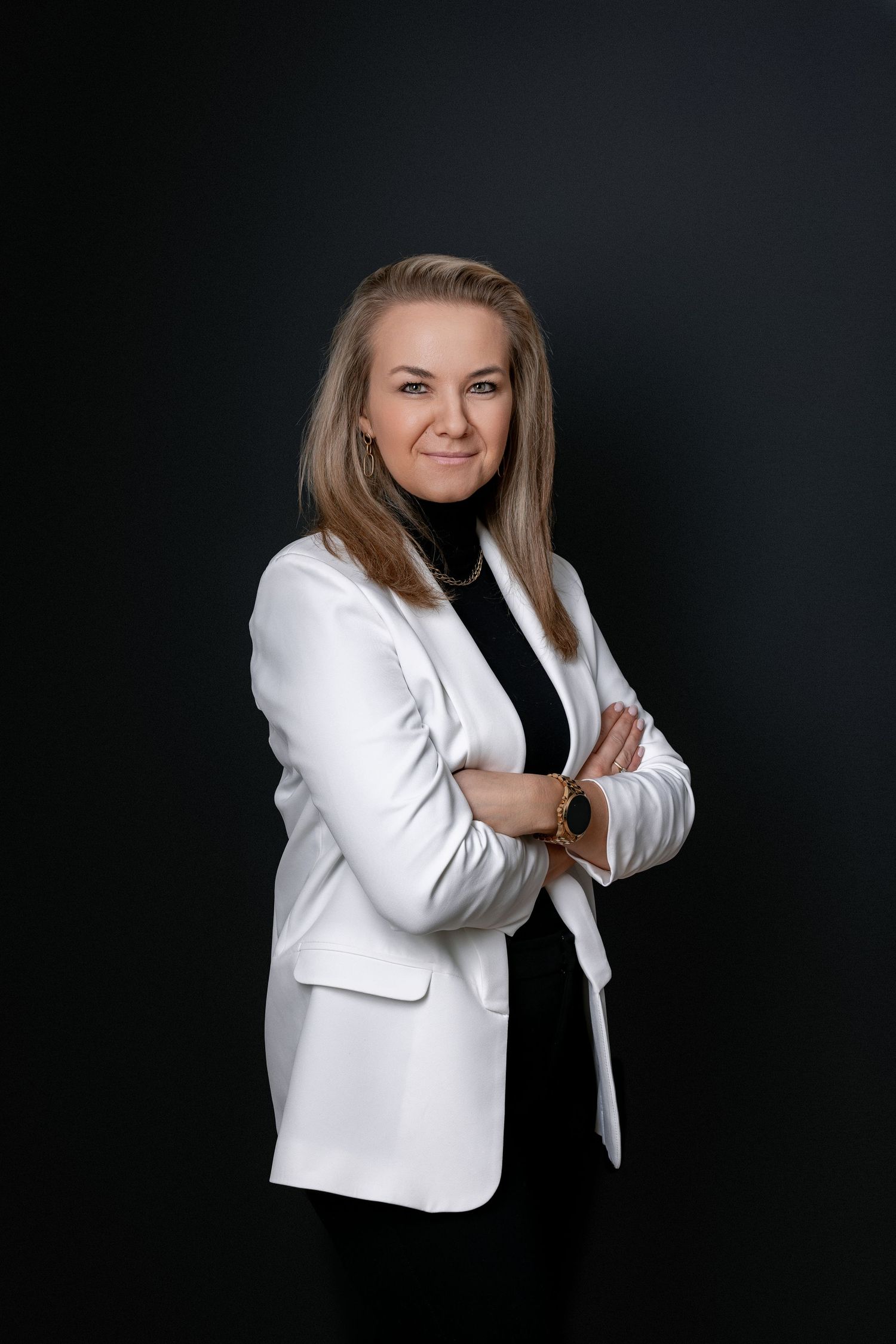 Professional portrait of someone in white blazer and black top against dark background.