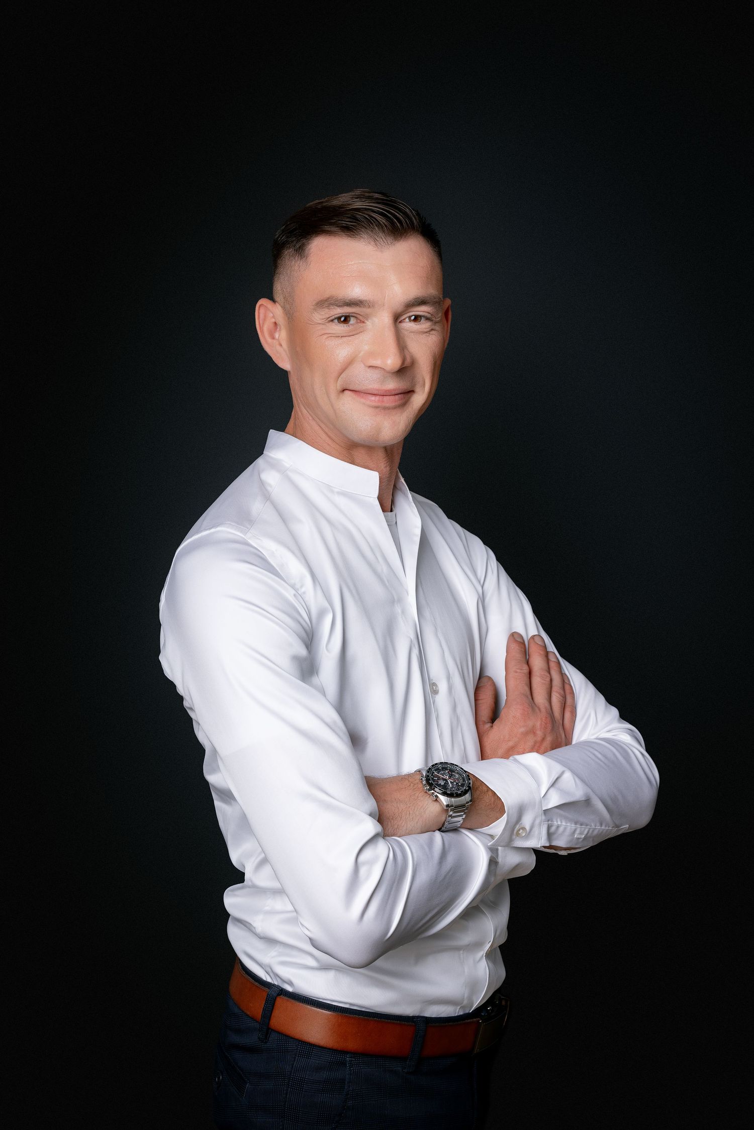 Professional studio portrait of someone in white button-down shirt with crossed arms.