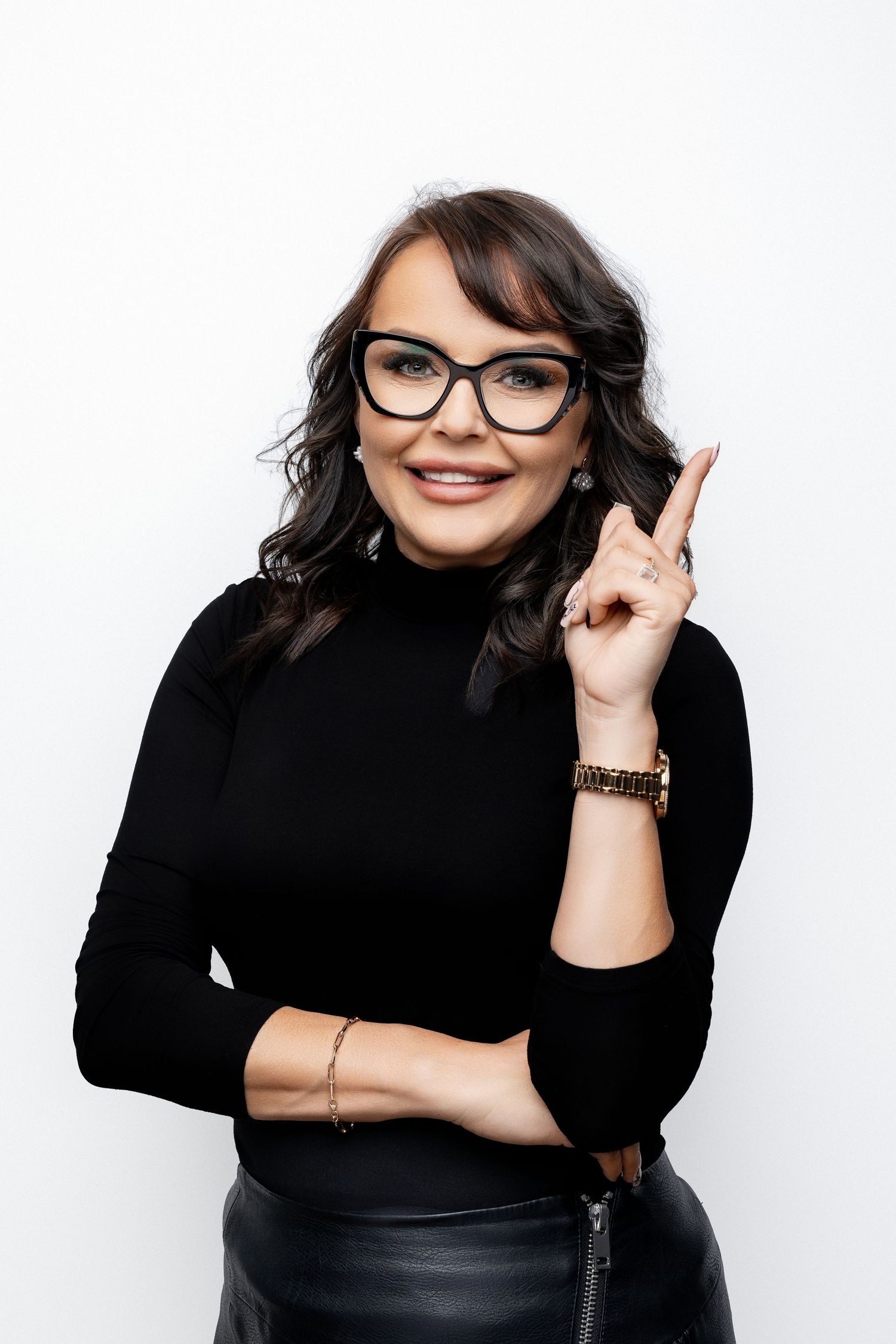 Professional in black turtleneck and glasses making pointing gesture against white background.