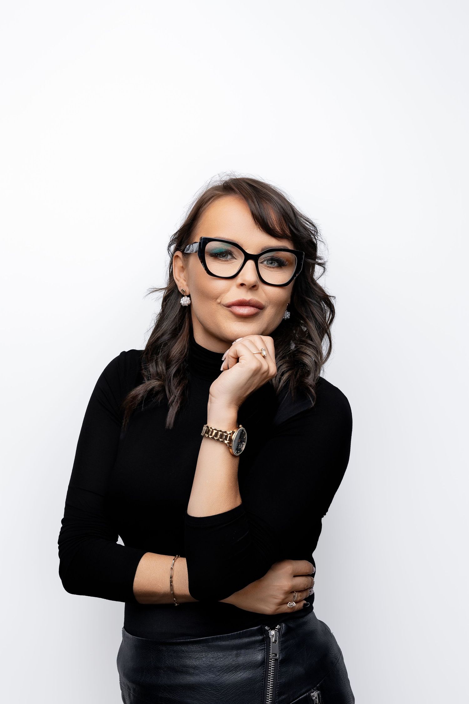 Stylish person in black turtleneck and glasses poses thoughtfully against white background.