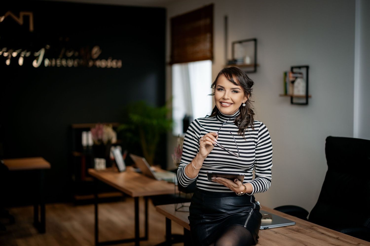 Professional in striped turtleneck holding digital tablet in modern office setting.