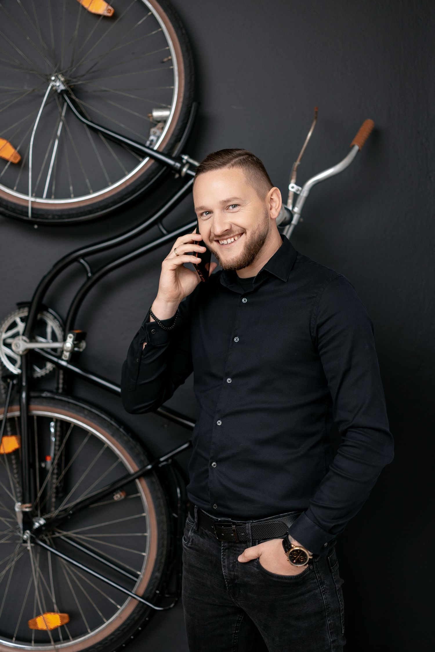 Professional in dark shirt talking on phone against wall with mounted bicycle.