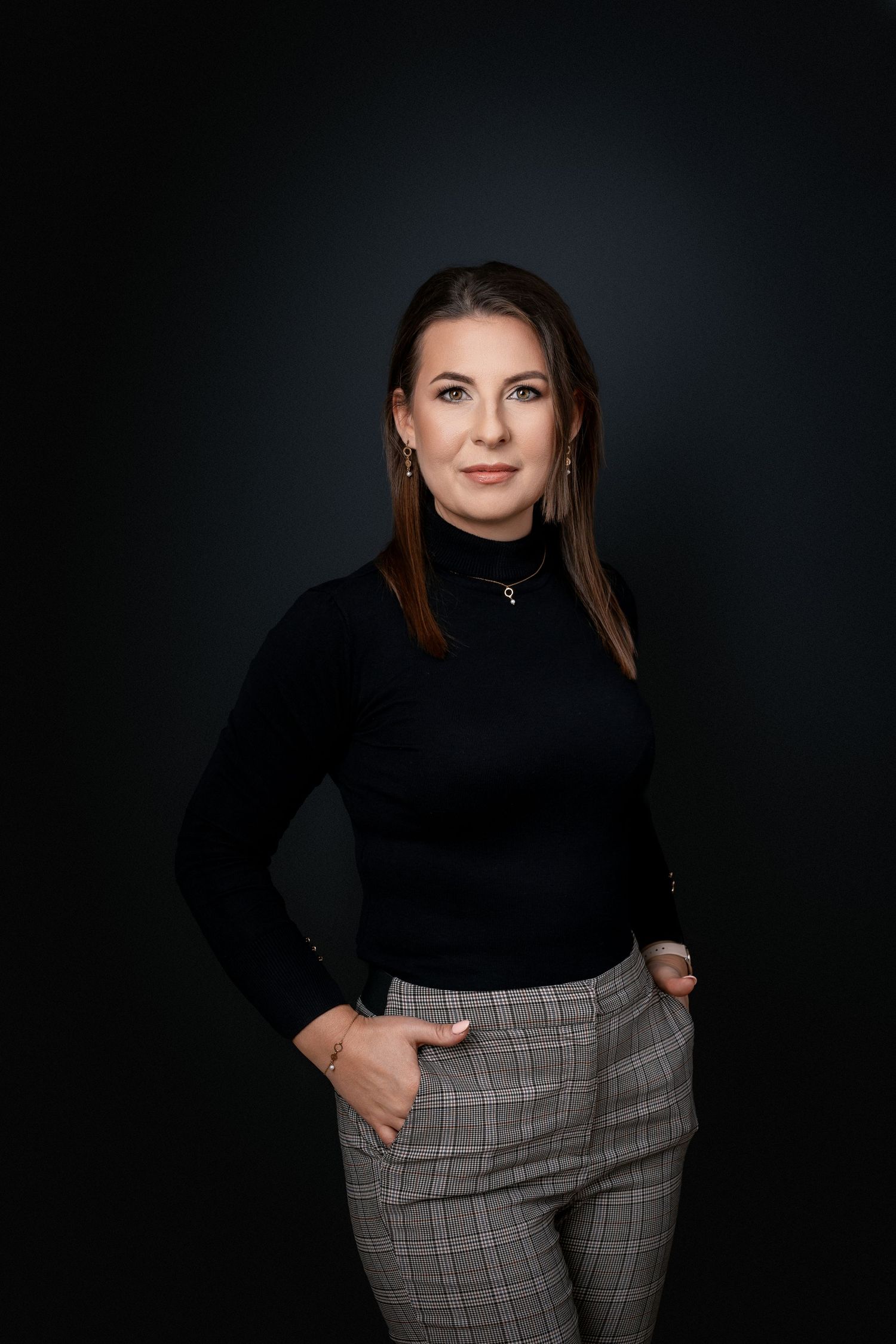 Professional headshot of someone wearing a black turtleneck and plaid pants against dark backdrop.