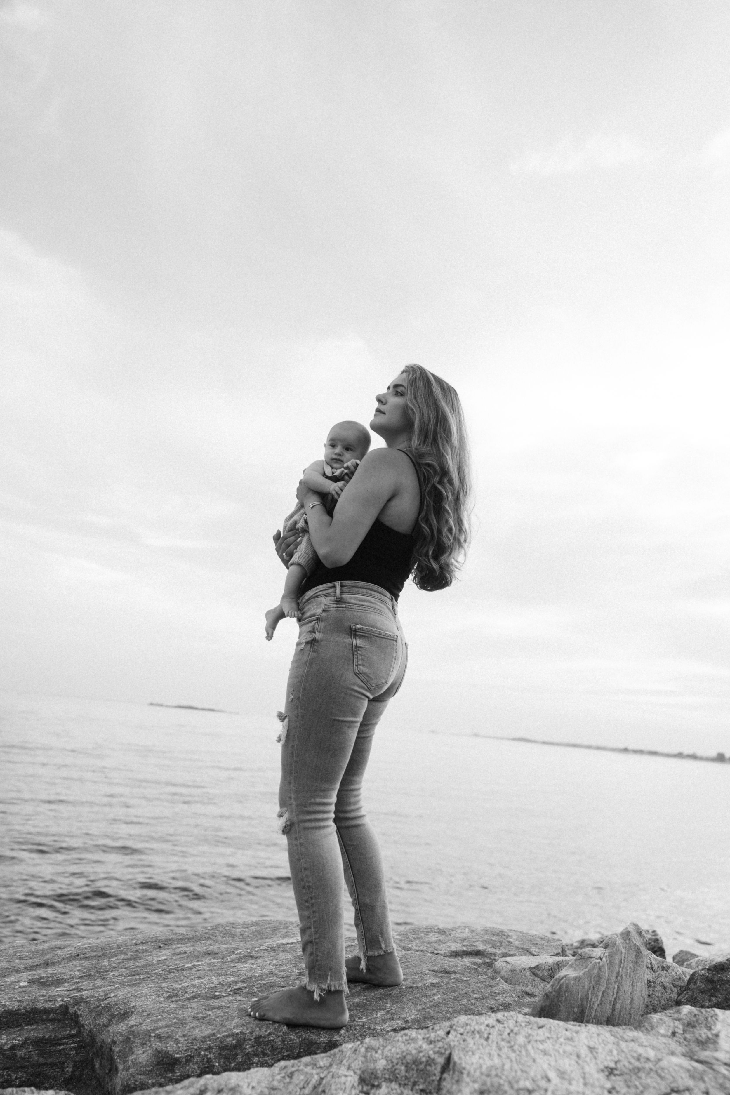 A scenic black and white photo of parent and baby standing on rocky shoreline overlooking the ocean.
