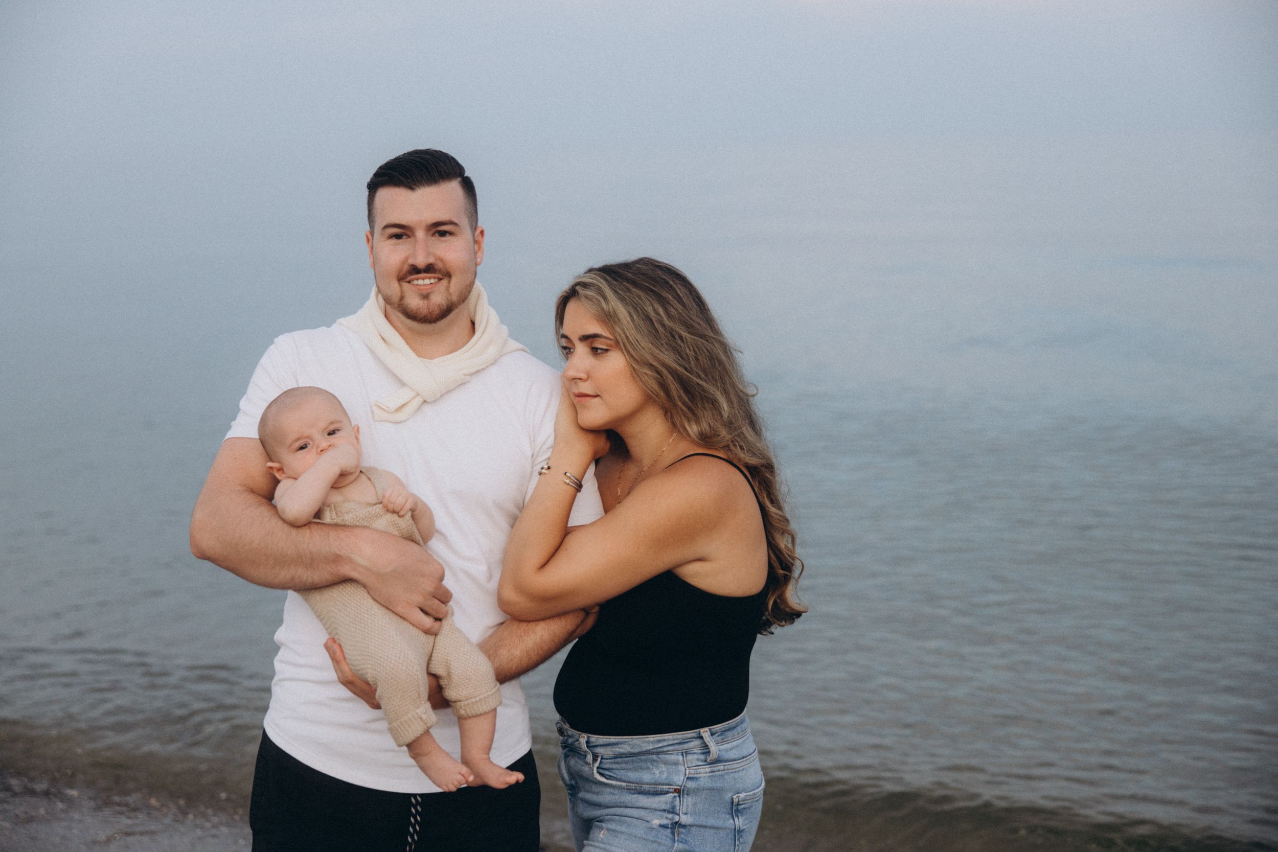 Family standing together on beach shore during golden hour with serene water behind them.