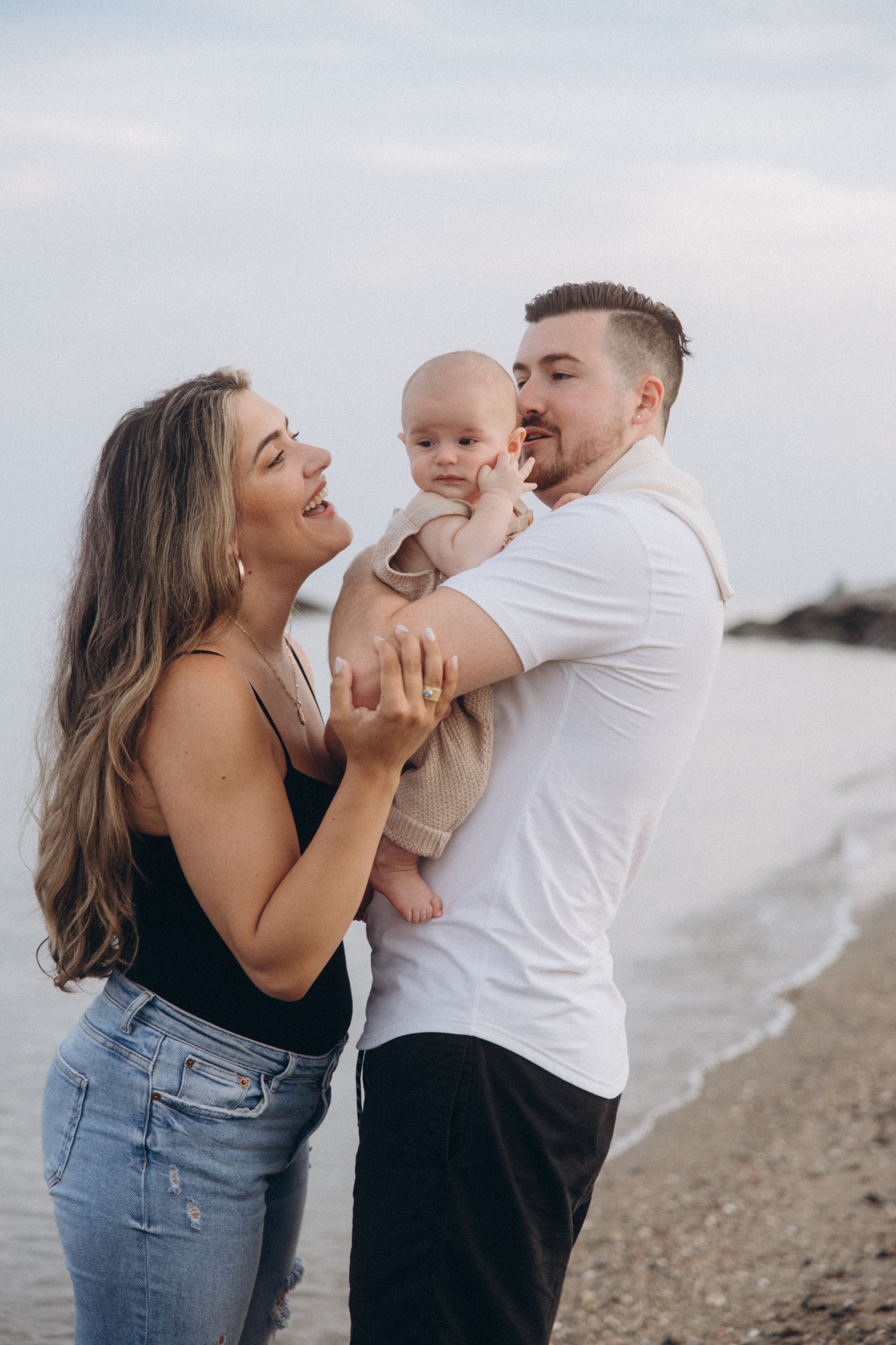 Joyful family moment captured on beach as parents interact with their baby.