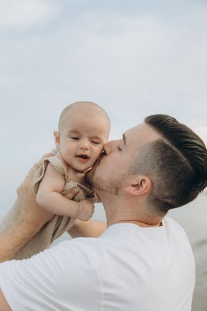 Sweet moment between parent and baby against soft cloudy sky background.