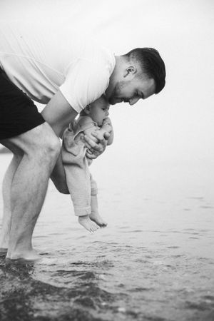 Black and white photo of someone dipping a baby's toes into the water.