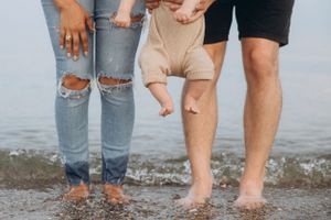 View of legs and feet as family stands in shallow beach water together.
