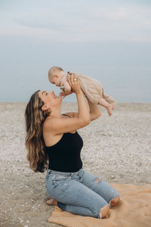 Mother lifting and playing with baby on a blanket at a rocky beach location.