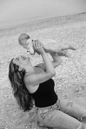 Black and white photo of mother and baby sharing a joyful moment on beach blanket.