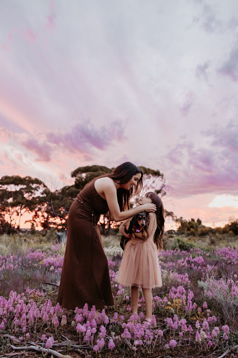 A touching scene unfolds in a lavender field as two people share an intimate moment under a dramatic purple sunset sky.