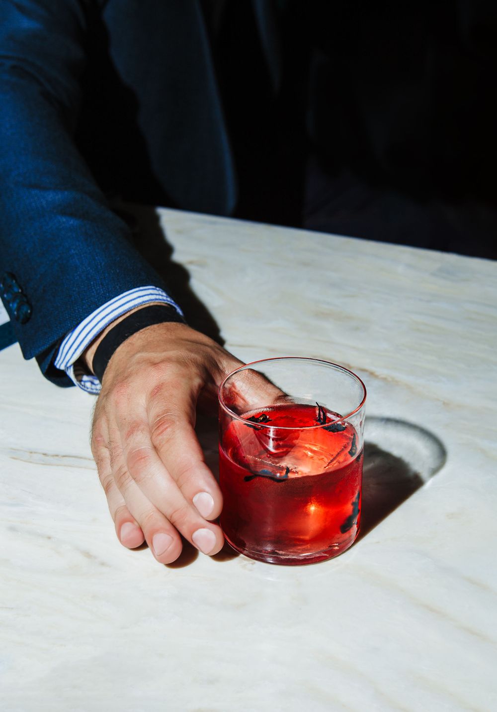 Hand holding red cocktail on white marble table surface.